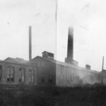 Black and White photograph showing many large brick industrial buildings and two prominent smokestacks