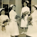 Colour photograph of four women, wearing vintage nursing uniforms, standing on steps, holding bouquets