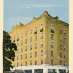 Colourized postcard of a large, six storey yellow brick building
