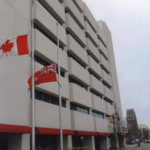 Exterior of a multi storey, white building. There is a Canadian flag and Ontario flag, both at half staff