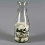 Colour photo of a glass bottle. It has Black lettering printed on it, reading Beaton's Dairy