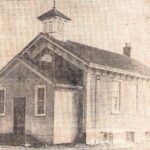 Grainy, black and white photo of a school house with large windows, a triangular roof, and a belvedere at the front