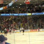 The Oshawa Generals, in their older red jerseys, face off against another team in yellow and white jerseys. The two teams are on the opposite end of the rink to where the photo was taken