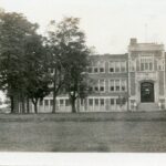 A black and white image of Centre Street Public school with a few trees in front of it. The image is taken from about 50 meters away from the entrance, so most of the 3 story school itself can be seen.