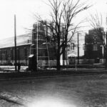 A black and white image of the RS McLaughlin Armoury, the year of the photograph is unknown but the roads seem unpaved and there are telephone lines in the background. Most of the building can be seen in the image, as it was taken around 40 meters northwest of the entrance.