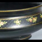 Close up detail of a black pottery bowl, featuring floral designs around the middle and a gold like around the rim and the base