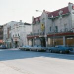 An image of the Lancaster Hotel in 1978, the image is taken at ground level across the street from the Hotel. 10 cars are seen parked along the side of the street, and a few neighbouring buildings can be seen further along the street from the hotel.