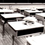 Black and white picture of rows of desks inside of a classroom