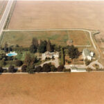 Aerial photograph of a house, pool and outbuildings surrounded by farmland