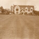 Sepia photo of a stone house. There is a large lawn in the foreground