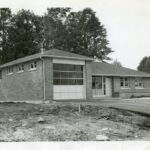 Black and white photograph of a rectangular building with a glass panel garage door.