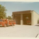 Rectangular brick building with two garage doors. One fire truck is parked in the driveway, another is parked in the garage.