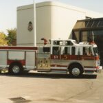 A fire truck in front of a white building beside a glass panel garage.