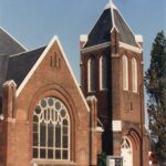 Colour photograph of a red brick church with a large, rounded window.