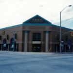 Colour photo of a large building. The building has two large pillars on either side of the front door, and the windows have a curved edge on top. The triangular sign at the top of the building reads "Wilson Furniture"