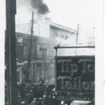 Black and white photo of a block of buildings on fire, taken from a second storey window