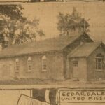 Sepia image of a long school house, with darker triangular roofs and a spire on top