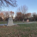 Colour photo of a park. There is a grey stone with "Chopin Park" engraved in it.